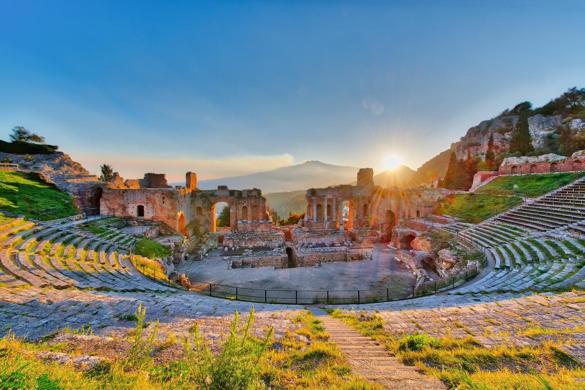 Ancient theatre of Taormina Sicily Italy  with Etna erupting volcano at sunset