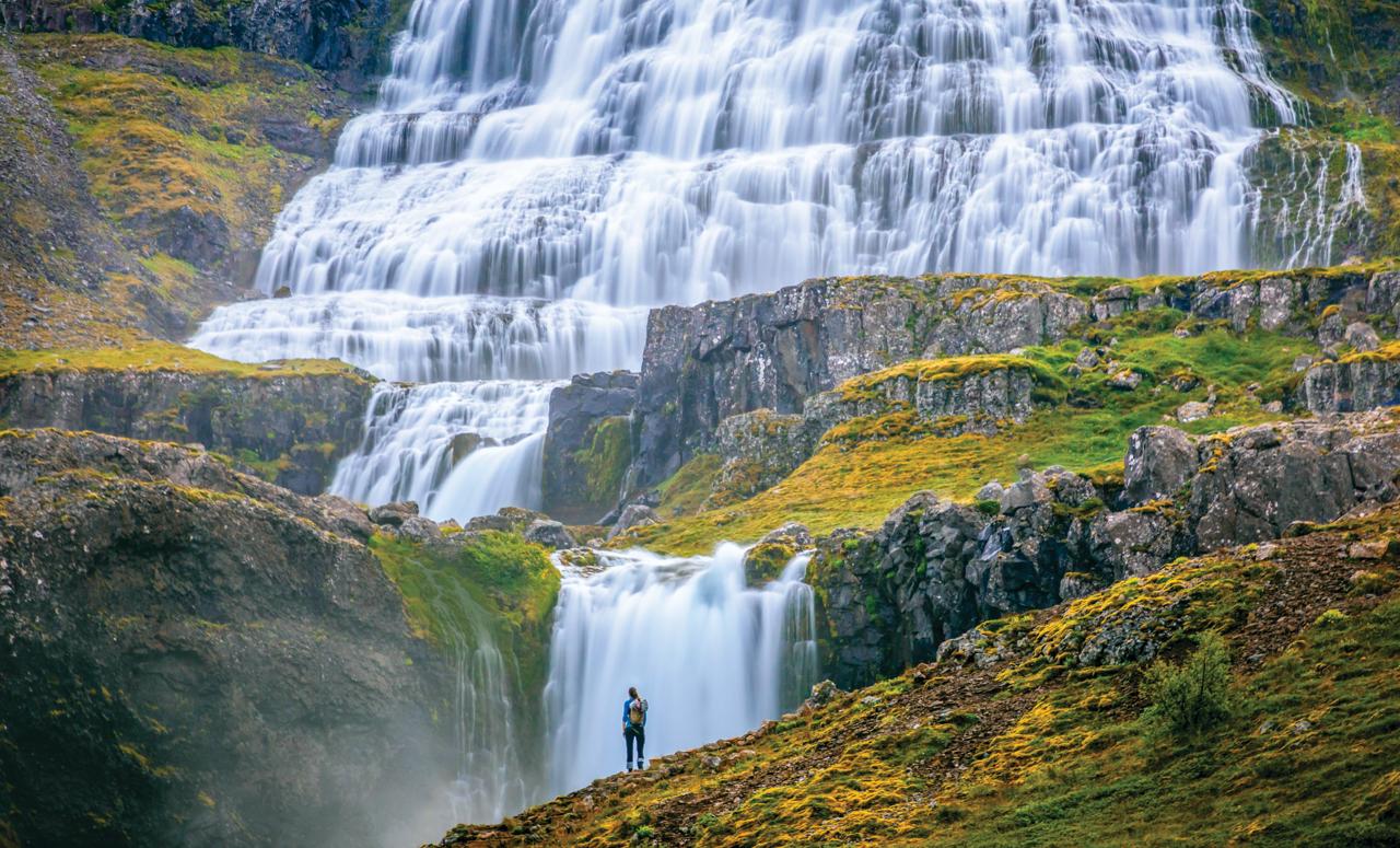 A hiker stands in front of the Dynjandi waterfall in Arnarfjörður in the Westfjords region of Iceland