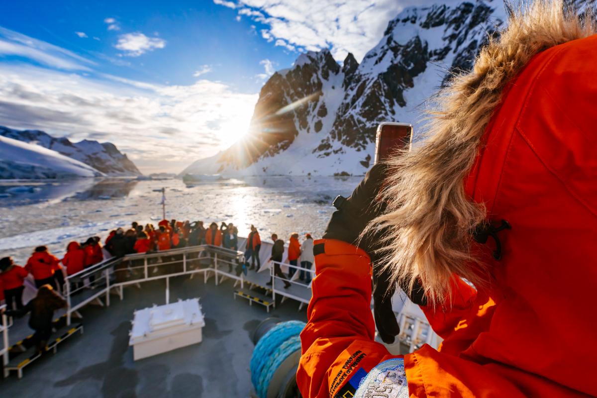 A guest photographs sunlight peeking through the Lemaire Channel from the ship National Geographic Explorer, Antarctic Peninsula