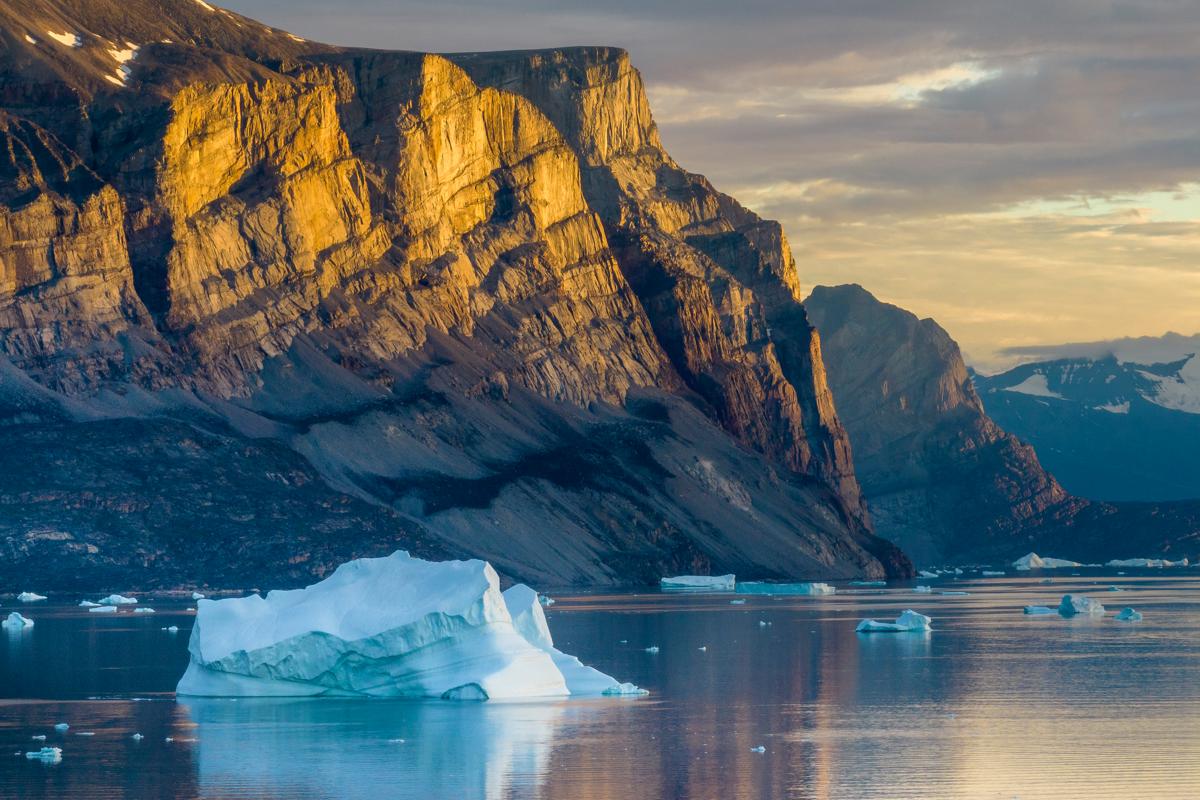 Greenland, Avannaata Municipality,  Setting midnight sun lights cliffs of Storøen Island along Alanguarqap Suvdlua strait near Uummannaq on summer evening