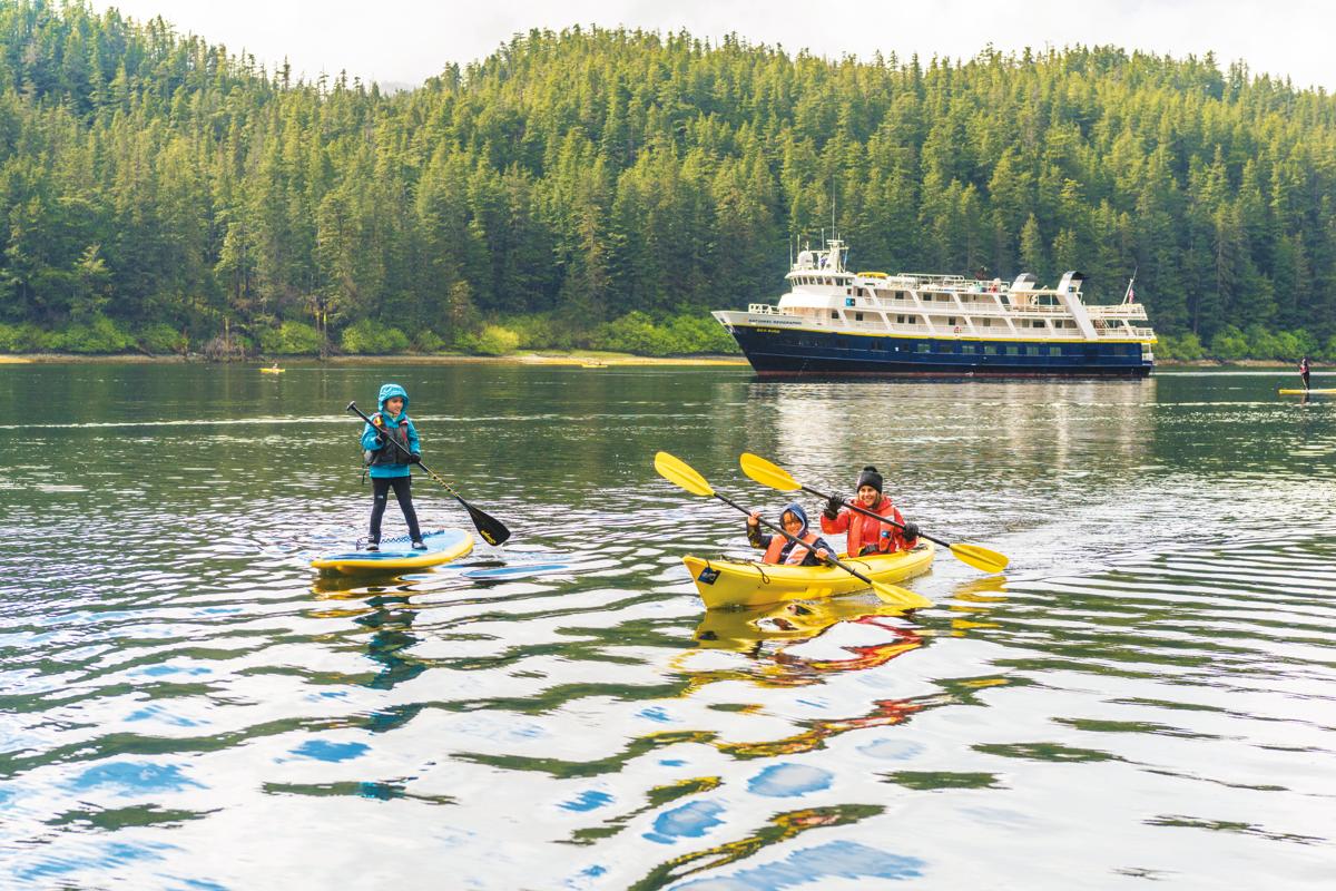 Young guests explore by stand up paddle board and kayak in Port Althorp, Alaska, USA